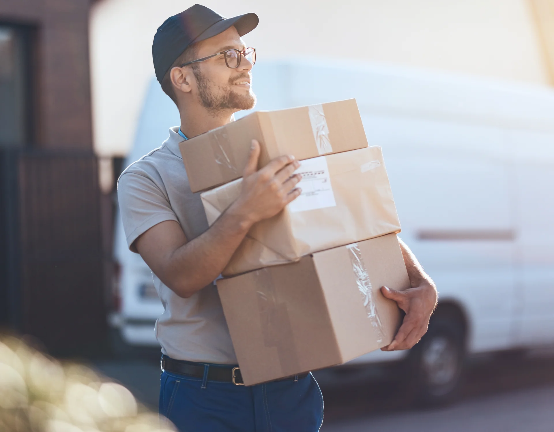 young-delivery-man-holding-stack-packages-while-making-home-delivery-residential-district