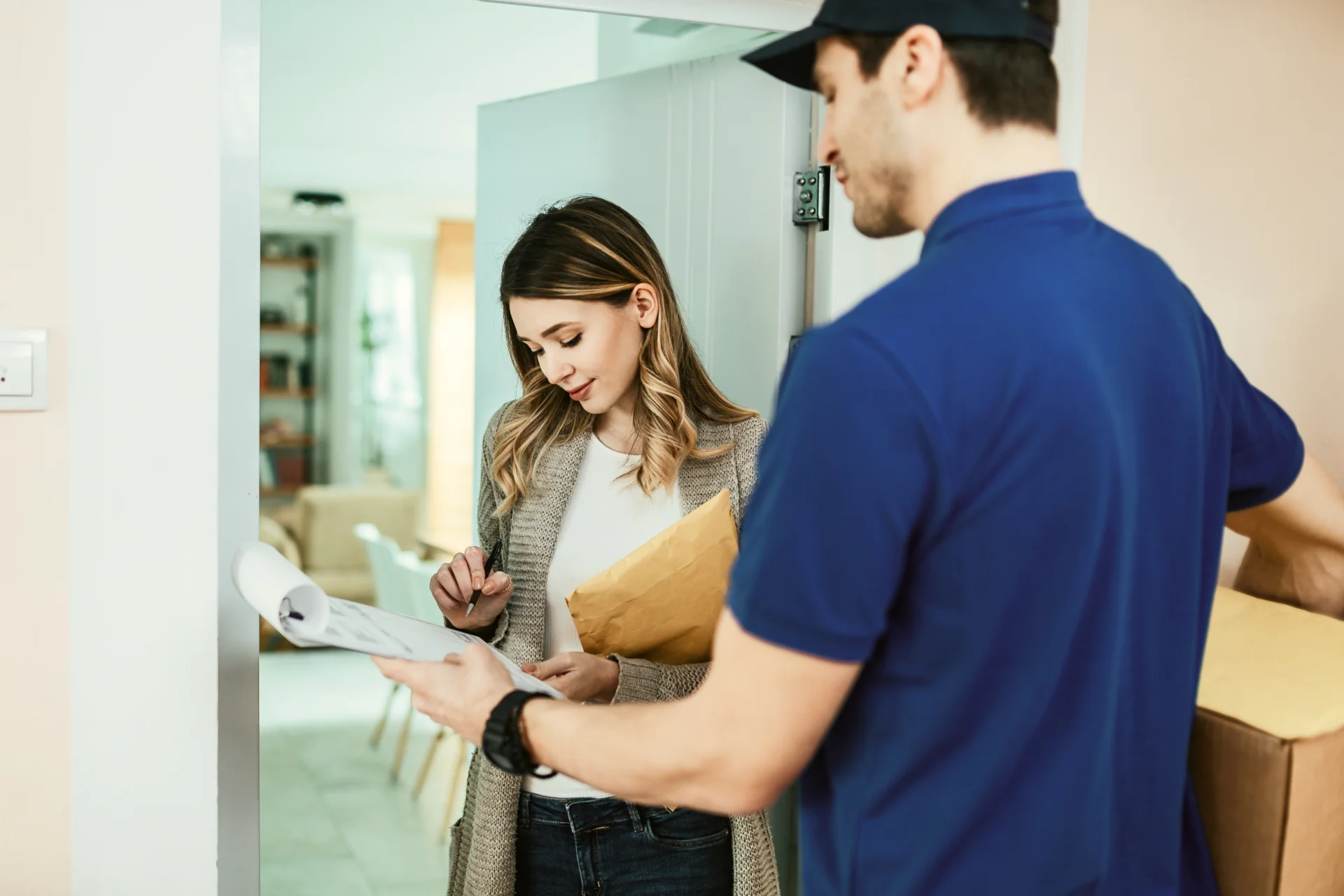 young-woman-signing-documents-while-receiving-home-delivery-from-courier